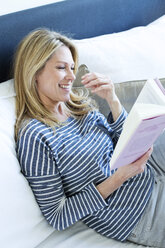 Woman sitting on couch reading a book - MAEF009988