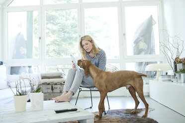 Frau mit ihrem Hund und digitalem Tablet zu Hause - MAEF010012