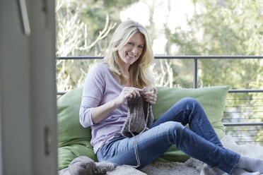 Blond woman sitting on balcony knitting - MAEF010020