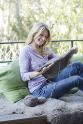 Blond woman sitting on balcony with knitting - MAEF010021