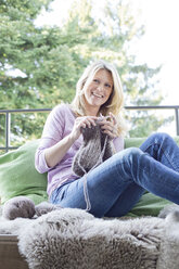 Blond woman sitting on balcony knitting - MAEF010023