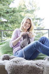 Blonde Frau sitzt auf dem Balkon und strickt - MAEF010023