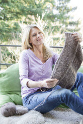 Blonde Frau sitzt auf dem Balkon und strickt - MAEF010025