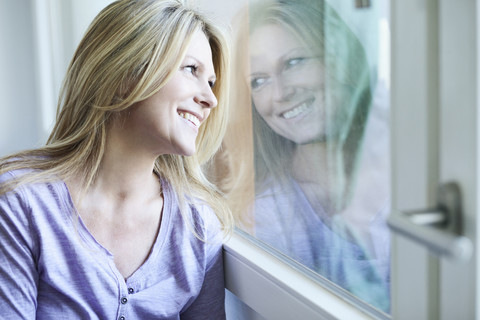 Blonde Frau schaut durch das Fenster, lizenzfreies Stockfoto