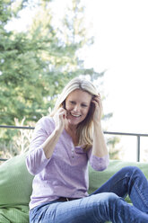 Blonde Frau sitzt auf dem Balkon und telefoniert - MAEF010041