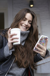 Germany, Dusseldorf, Young woman with coffee cup using smart phone - RHF000681