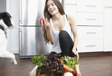 Glückliche junge Frau in der Küche mit einer Kiste voll frischem Gemüse - RHF000693