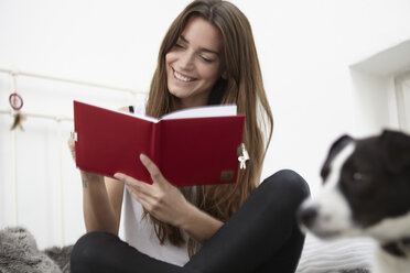 Young woman sitting on bed with dog writing diary - RHF000702