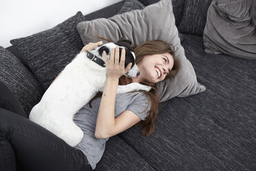 Young woman playing with dog on couch - RHF000716