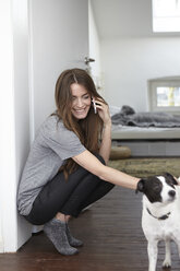 Junge Frau mit Hund zu Hause beim Telefonieren - RHF000743