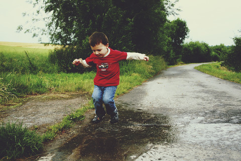Kleiner Junge, der in eine Pfütze springt, Erkrath, Nordrhein-Westfalen, Deutschland, lizenzfreies Stockfoto