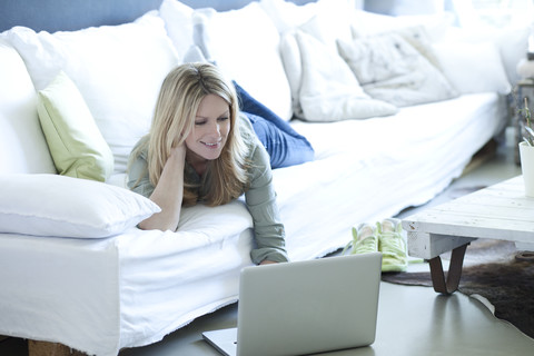 Frau entspannt auf Couch mit Laptop, lizenzfreies Stockfoto