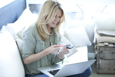Smiling blond woman with laptop using online banking - MAEF010060