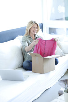 Woman sitting on couch unpacking online shopping purchase - MAEF010075