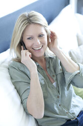 Portrait of smiling woman sitting on couch telephoning with smartphone - MAEF010073