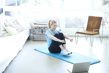 Woman with laptop exercising on gym mat in living room - MAEF010080