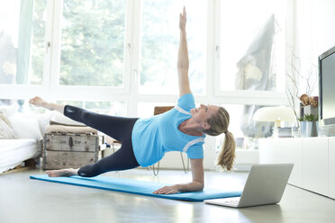 Woman with laptop exercising on gym mat in living room - MAEF010091