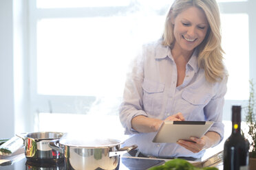 Frau mit digitalem Tablet beim Kochen in der Küche - MAEF010109