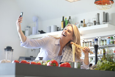 Glückliche Frau, die in der Küche kocht und ein Selfie macht - MAEF010113