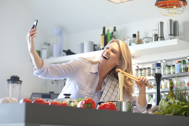 Happy woman cooking in kitchen taking a selfie - MAEF010113