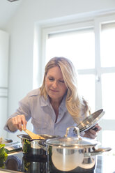 Woman cooking in kitchen enjoying smell from cooking pot - MAEF010158