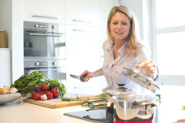 Lächelnde Frau beim Kochen in der Küche - MAEF010117