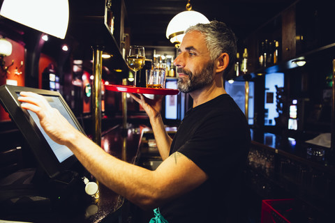 Kellner hält Tablett mit Getränken in einem irischen Pub, während er an der Kasse arbeitet, lizenzfreies Stockfoto