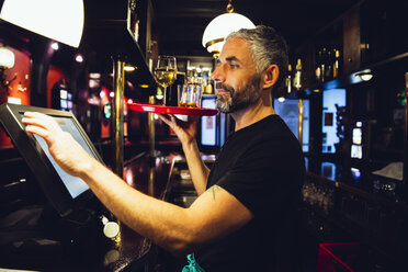 Kellner hält Tablett mit Getränken in einem irischen Pub, während er an der Kasse arbeitet - MBEF001383