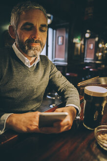Porträt eines Mannes, der am Tresen einer Kneipe sitzt und sein Smartphone benutzt - MBEF001354