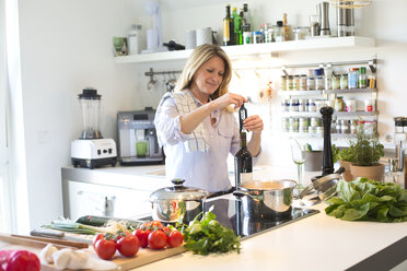 Smiling woman cooking in kitchen opening a bottle of wine - MAEF010159