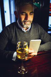 Porträt eines Mannes, der am Tresen einer Kneipe sitzt und sein Smartphone benutzt - MBEF001359