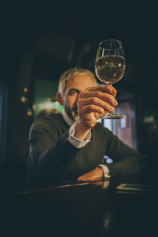 Mann sitzt am Tresen einer Kneipe und beobachtet ein Glas Weißwein, lizenzfreies Stockfoto