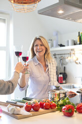 Lächelnde Frau in der Küche stößt mit einem Glas Rotwein an - MAEF010160