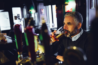 Mann sitzt am Tresen einer Kneipe und trinkt Bier - MBEF001373