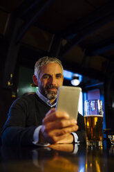 Man sitting at counter of a pub looking at his smartphone - MBEF001364