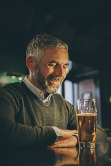 Lächelnder Mann sitzt am Tresen einer Kneipe mit einem Glas Bier - MBEF001367