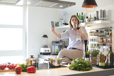 Frau in der Küche mit einem Glas Rotwein macht ein Selfie - MAEF010127
