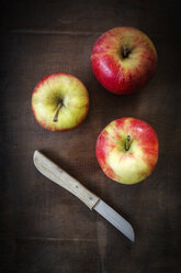 Drei Äpfel und Küchenmesser auf dunklem Holz - EVG001572