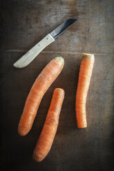 Drei Karotten und ein Küchenmesser auf dunklem Holz - EVG001582