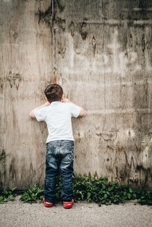 Kleiner Junge, der durch ein Loch in der Baustellenwand schaut, Stuttgart, Baden-Württemberg, Deutschland - SBDF002786