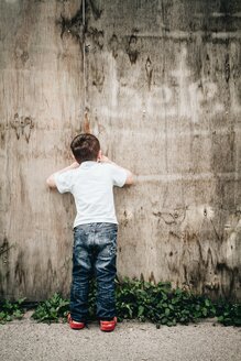 Little boy, looking through hole in building site wall, Stuttgart, Baden-Württemberg, Germany - SBDF002786