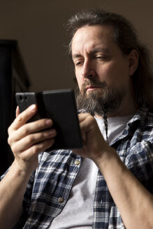 Mann mit geflochtenem Bart schaut auf sein Smartphone - MIDF000242