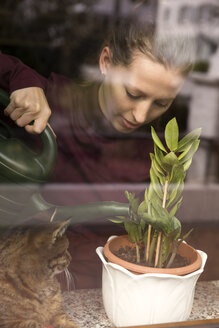 Frau mit Katze gießt Pflanze am Fenster - MIDF000248