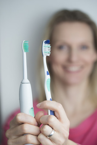Frau hält klassische und elektrische Zahnbürste, lizenzfreies Stockfoto