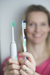 Frau hält klassische und elektrische Zahnbürste - CHPF000128
