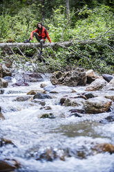 Österreich, Altenmarkt-Zauchensee, junge Wanderin sitzt auf Totholz über einem Fluss - HHF005253