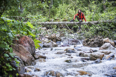 Österreich, Altenmarkt-Zauchensee, junge Wanderin sitzt auf Totholz über einem Fluss - HHF005254