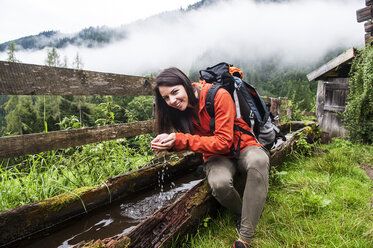 Österreich, Altenmarkt-Zauchensee, junge Wanderin rastet an einem Springbrunnen - HHF005259