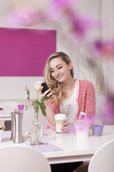 Lächelnde blonde Frau, die in einem Café sitzt und ihr Smartphone benutzt - JUNF000286