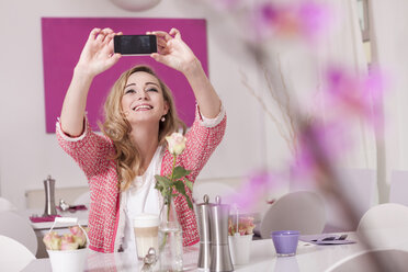 Lächelnde blonde Frau sitzt in einem Café und macht ein Selfie mit Smartphone - JUNF000287